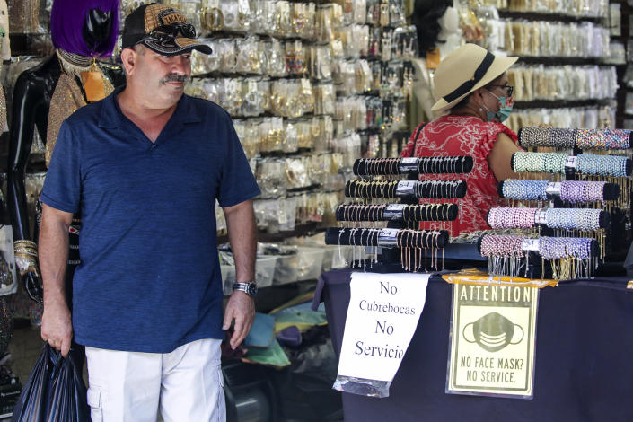 Customers in a store posting two signs, one in Spanish, and one in English, saying: No Face Masks, No Service.